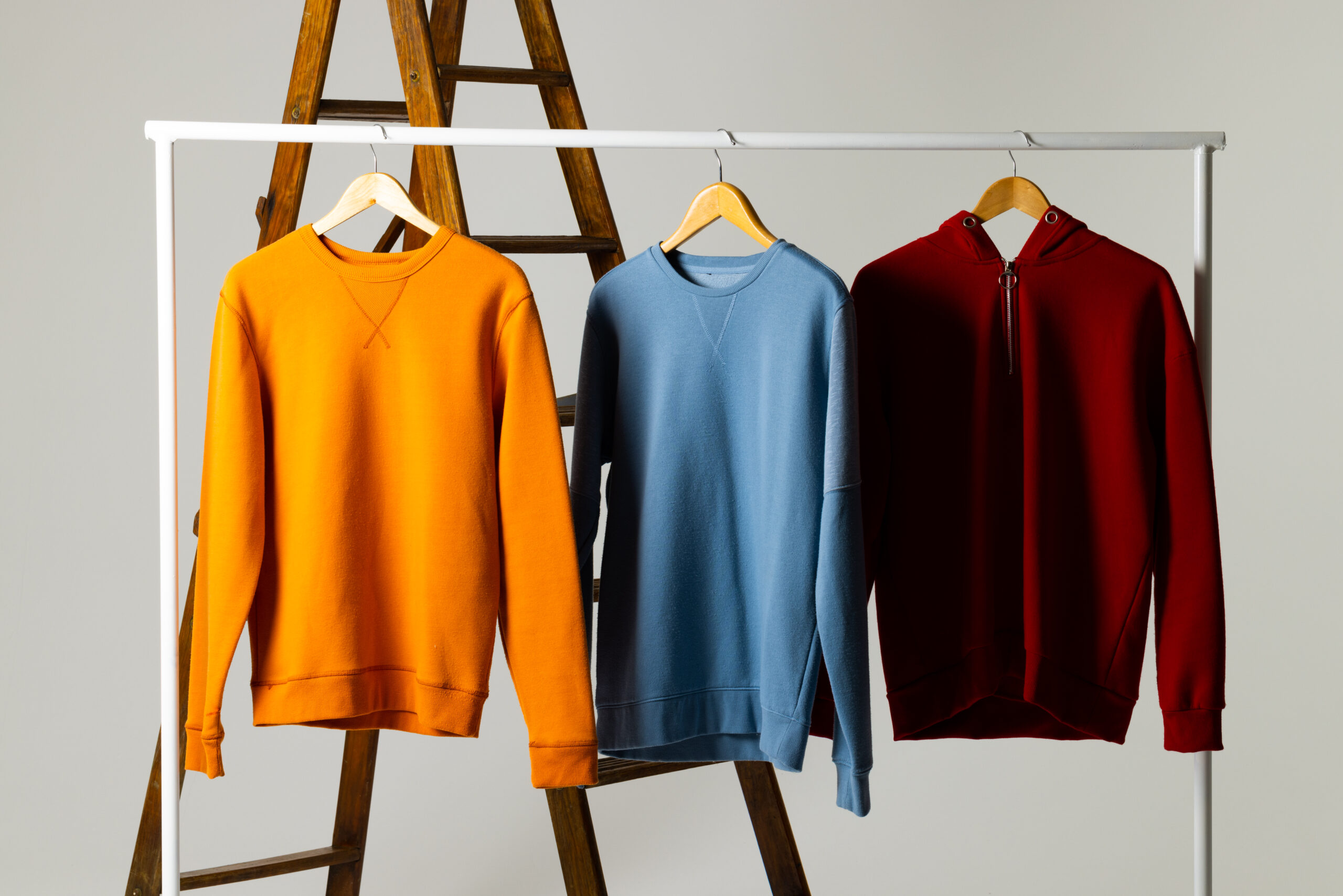 Coloured sweatshirts displayed on ladder and copy space on white background. Clothing, fashion and retail concept.